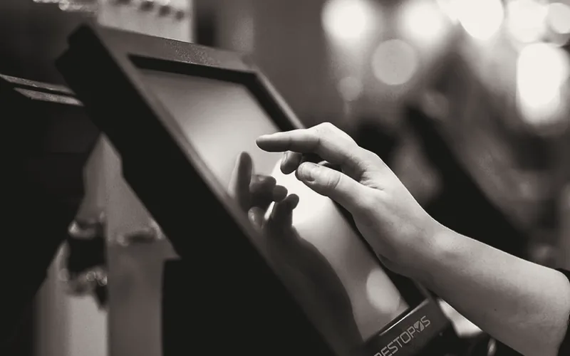 A hand touching the RestoPOS touchscreen till